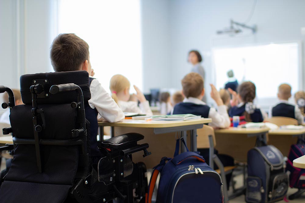 Back view of a child in wheelchair in his classroom looking at the teacher